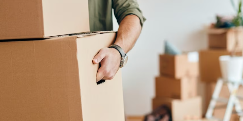 man carrying multiple cardboard boxes from a room full of cardboard boxes